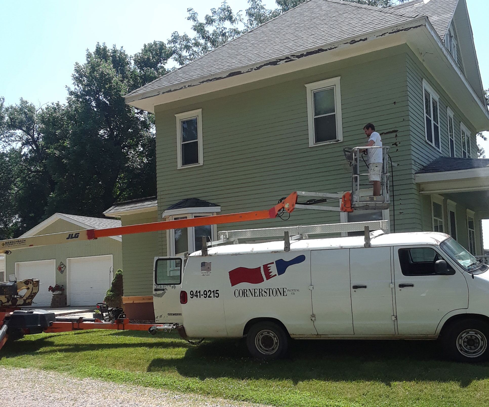 Cornerstone painter working a two-story exterior from a boom lift, the lettered company van below